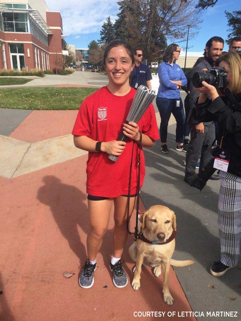 Letticia Martinez posing with her seeing-eyed-dog while wearing a red shirt and holding the Olympic Torch